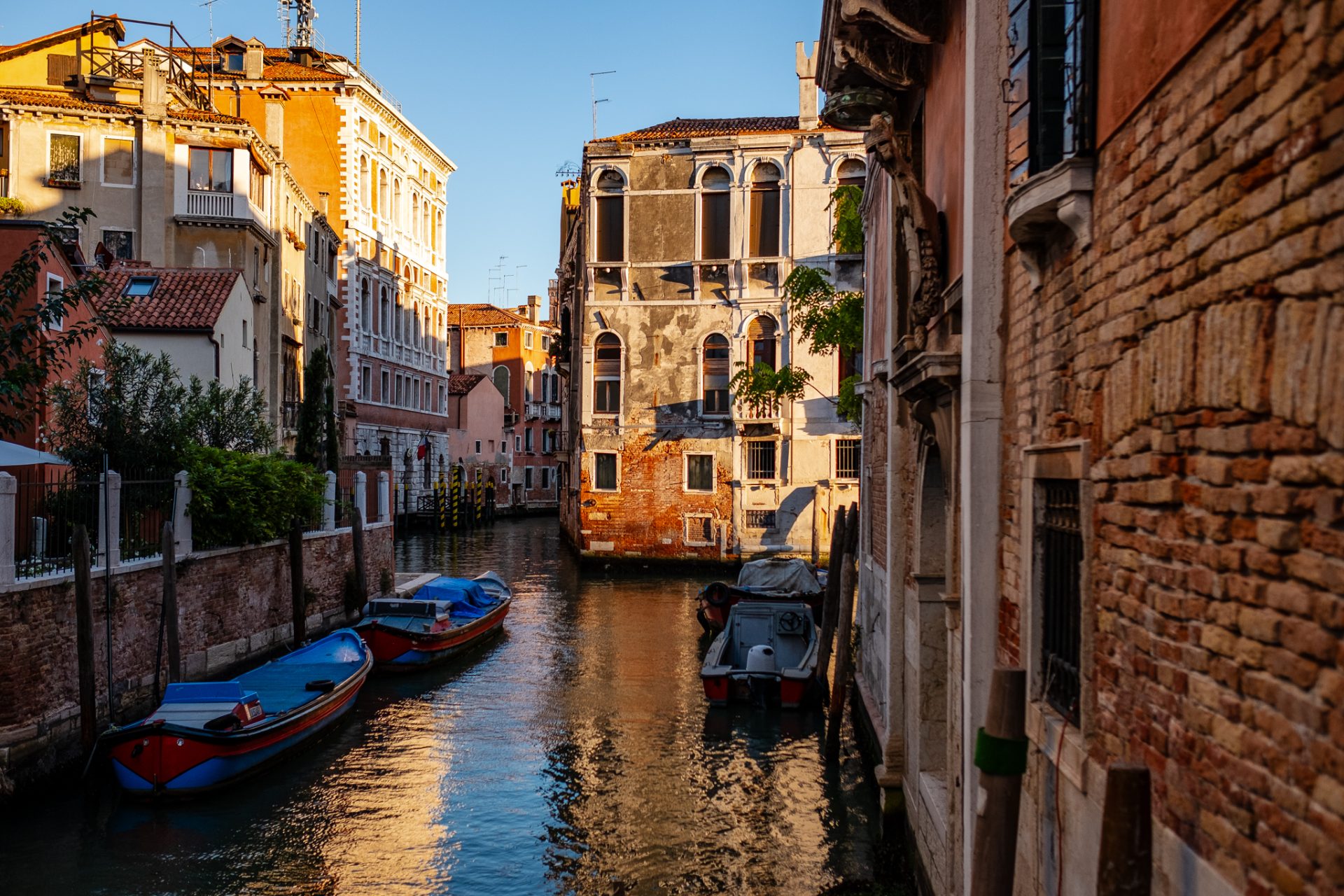 Color photo of a quiet Venice canal at golden hour with moored boats and warm light on the buildings.