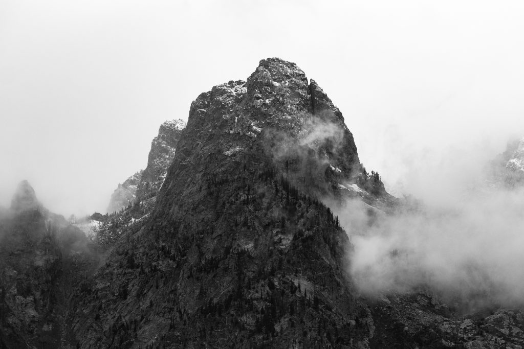 Black and white photo of a dark, rugged Grand Teton peak with a wisp of cloud crossing its face.