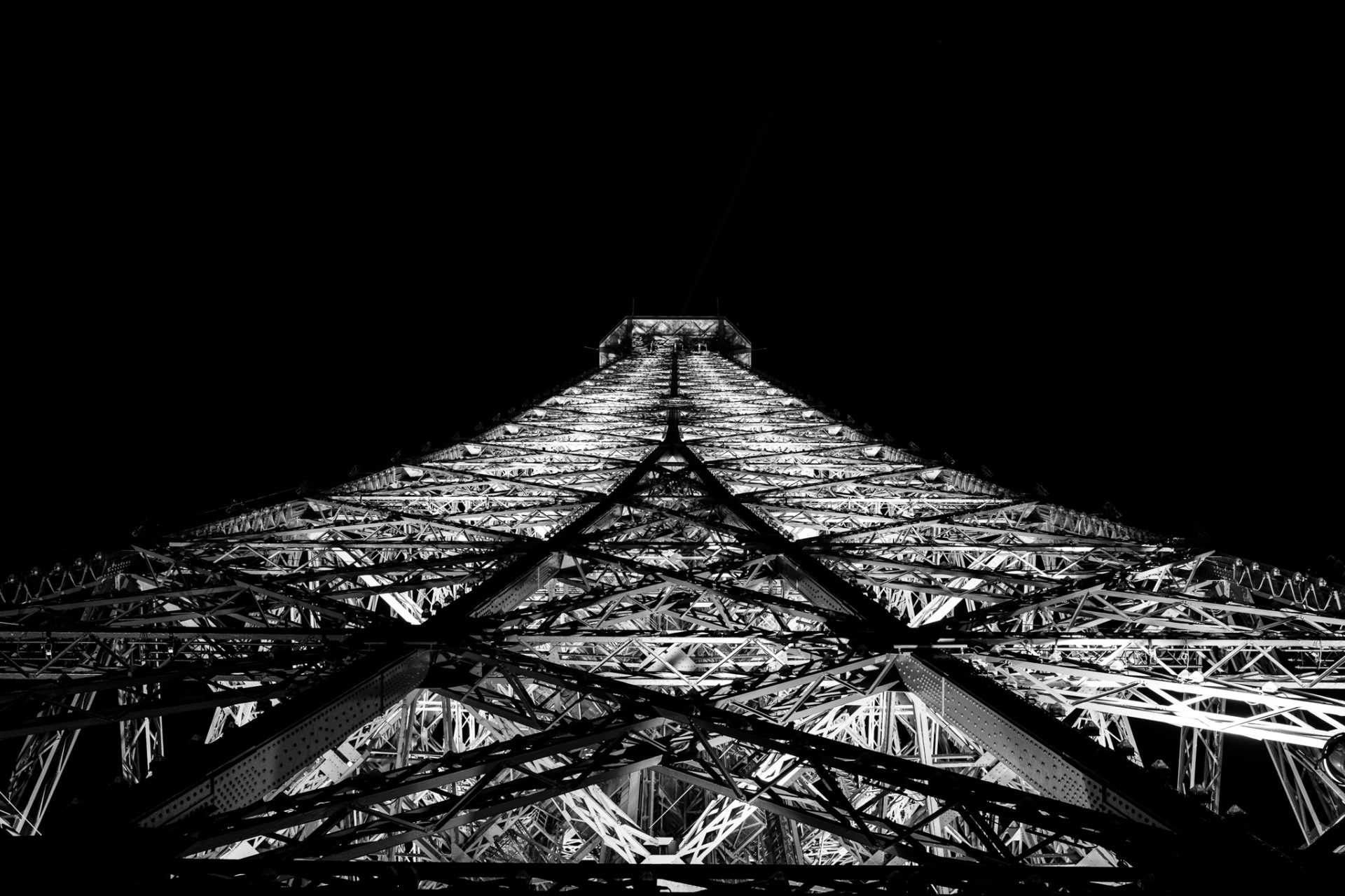 Black and white photograph shot straight up the central axis of the Eiffel Tower, symmetrical iron latticework converging toward the top.